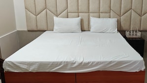 A neatly made bed with a padded headboard, white bedding, and a small woven basket on the nightstand. - Amantaran Farm Retreat (Varanasi)