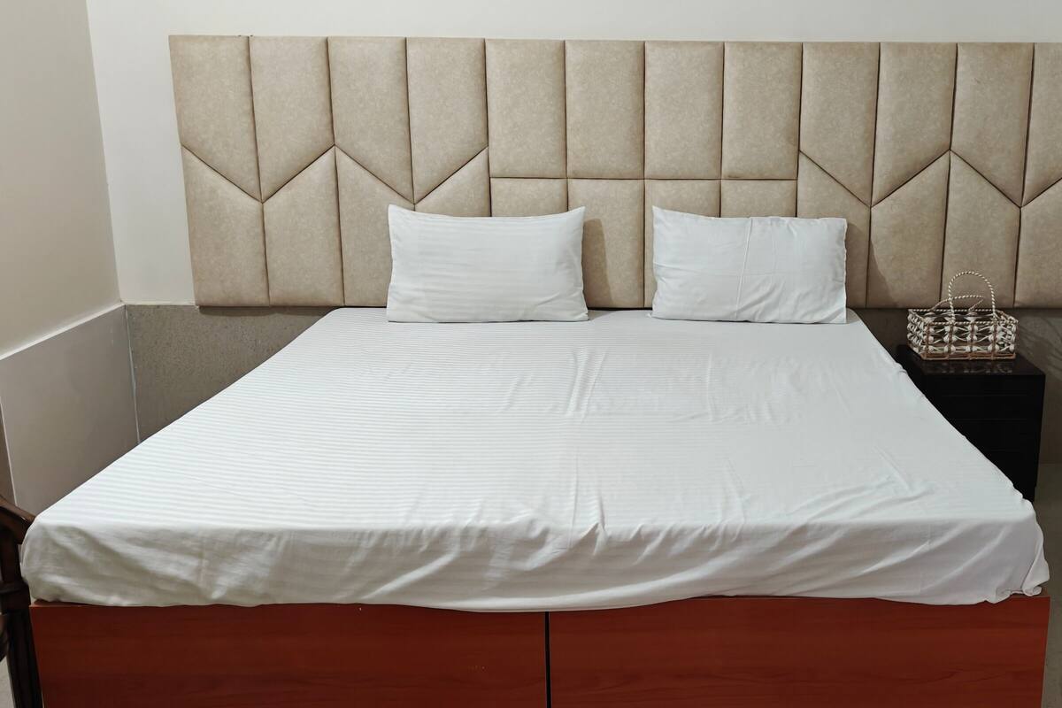 Una cama bien hecha con cabecera acolchada, ropa de cama blanca y una pequeña cesta tejida en la mesita de noche.