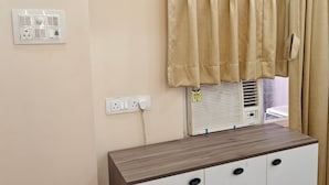 A room with a wooden dresser, a power outlet, a heater, and beige curtains. - Amantaran Farm Retreat (Varanasi)