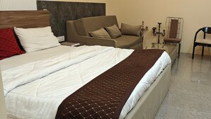 A hotel room with a large bed, a sofa, a chair, and a small table with a candelabra. - Amantaran Farm Retreat (Varanasi)