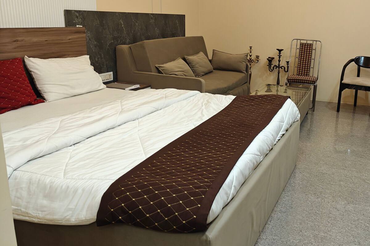 Habitación de hotel con una cama grande, un sofá, una silla y una pequeña mesa con un candelabro.