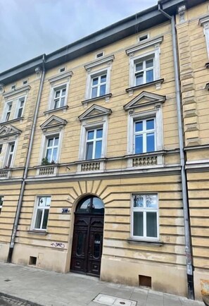 Ein mehrgeschossiges Gebäude mit einer symmetrischen Fassade, großen Fenstern und einem zentralen Eingang mit einem dekorativen Bogen.