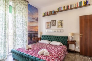 A bedroom with a green upholstered bed, a bookshelf with books, framed artwork, and a large window with curtains. - Spacious 80 sqm apartment with a balcony, comfortably accommodating up to 4 people, located on the third floor of a building with an elevator. The property is located in the charming Centro neighborhood, in the heart of Livorno's nightlife, just steps fr (Livorno)