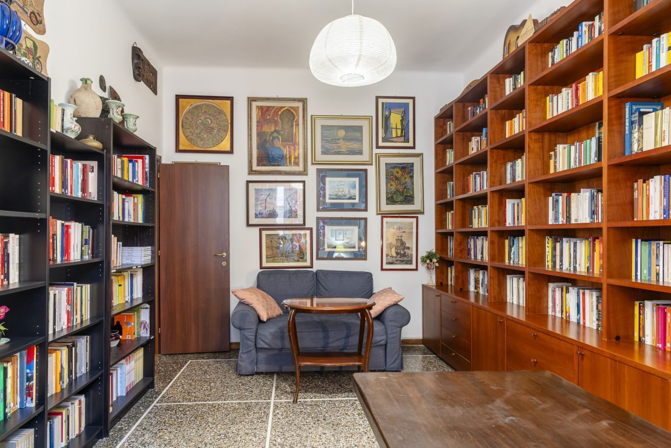 Ett bibliotek med bokhyllor, en soffa, ett soffbord och inramade konstverk på väggarna.