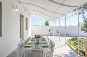An outdoor patio with a glass table set for dining, surrounded by chairs, under a white canopy. - Villatrullo Melograno - Villa with pool in Salento (Torre Suda)