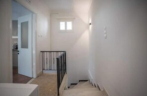 Un pasillo estrecho con una escalera, un ventanal pequeño y una puerta que da a una zona de cocina.