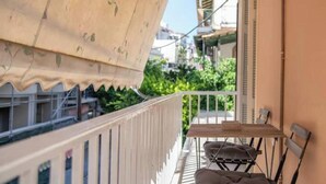 A balcony with a table and chairs, a white railing, and a view of greenery and buildings. - Charming Couples' Apartment in Zakynthos Town (Zakinthos)