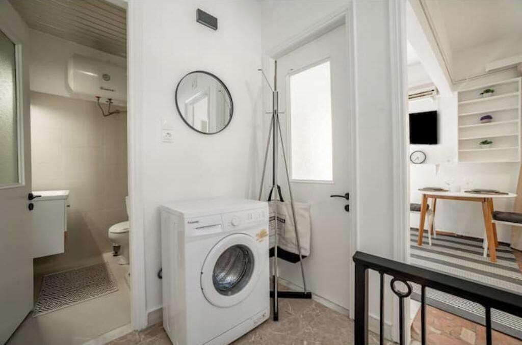 Een wasruimte met een wasmachine, een droogrek en een spiegel aan de muur.