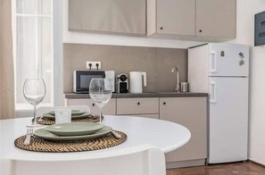 Una cocina moderna con una mesa blanca preparada para comer, un refrigerador y un microondas.