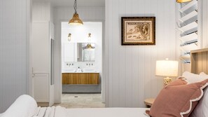 Ein Hotelzimmer mit einem Bett, einem Nachttisch mit Lampe, einem gerahmten Bild an der Wand und Blick ins Bad.
