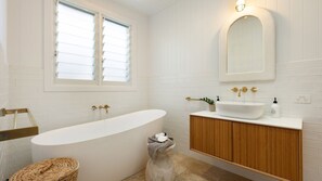 A bathroom with a freestanding bathtub, a vanity with a sink, a mirror, and a window with blinds. - Welcome to Pineapple House, a relaxed take on luxury in the heart of Byron Bay, where colonial plant (Byron Bay)