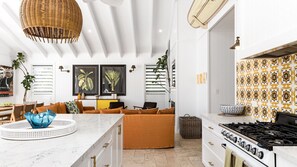 Una cucina moderna con un piano cottura bianco, un'area pranzo con un divano marrone e un ampio lampadario in vimini.