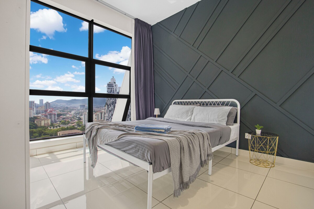 A modern bedroom with a city view, a bed with a grey and white headboard, a small bedside table with a plant, and a geometric-patterned wall.