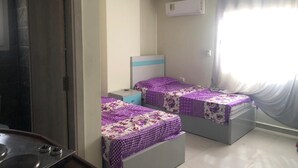 A room with two beds, a small table, a window with curtains, and an air conditioning unit.