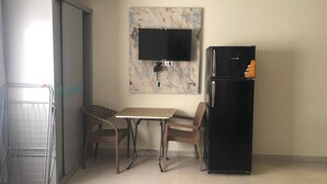 A compact kitchen with a dining table, chairs, a refrigerator, and a wall-mounted TV.