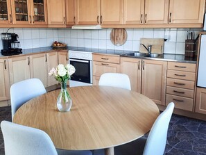 Una cocina moderna con armarios de madera, una mesa redonda para comer y un jarrón con flores.