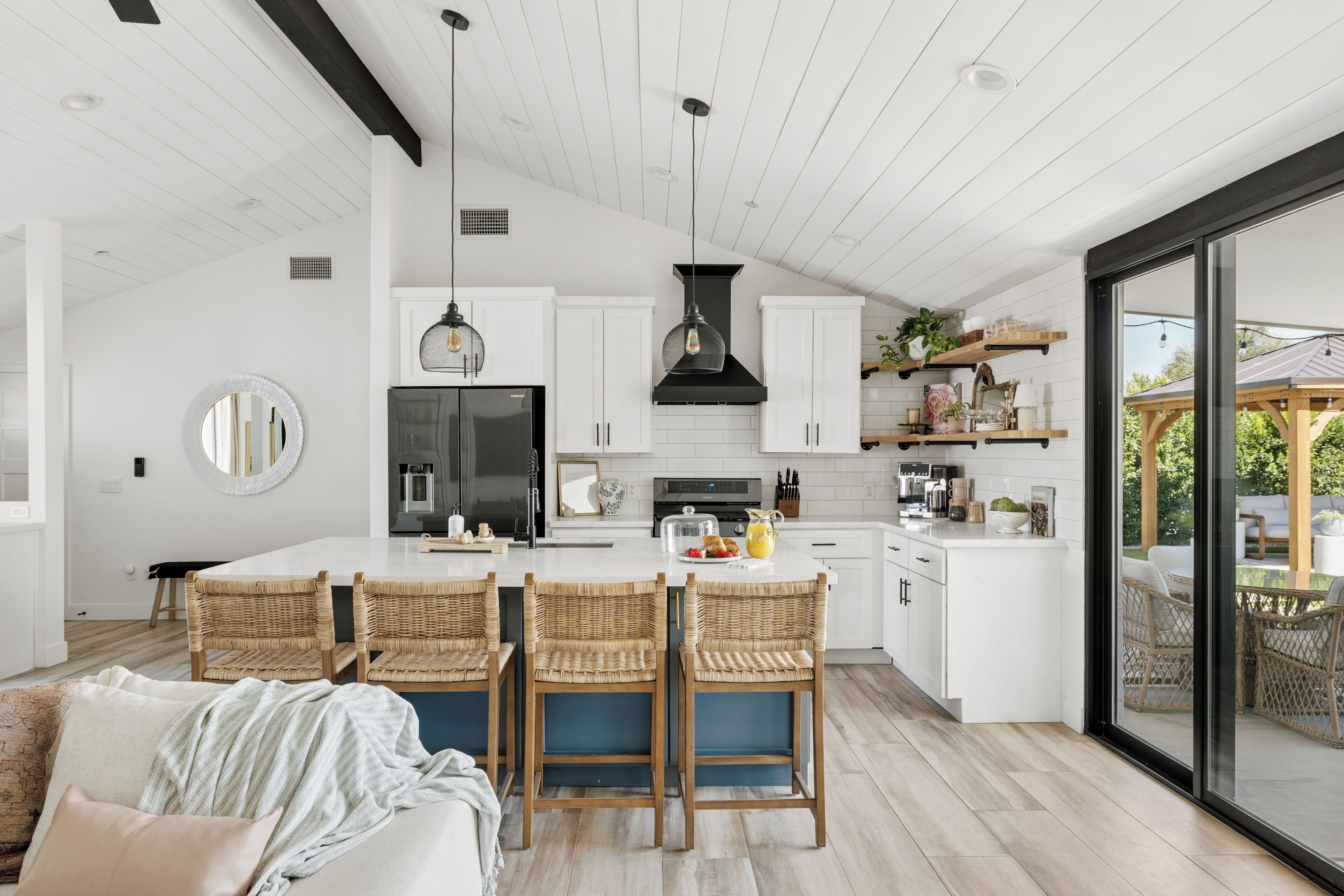 A modern kitchen with white cabinetry, a central island with bar stools, and a large sliding glass door leading to an outdoor area.