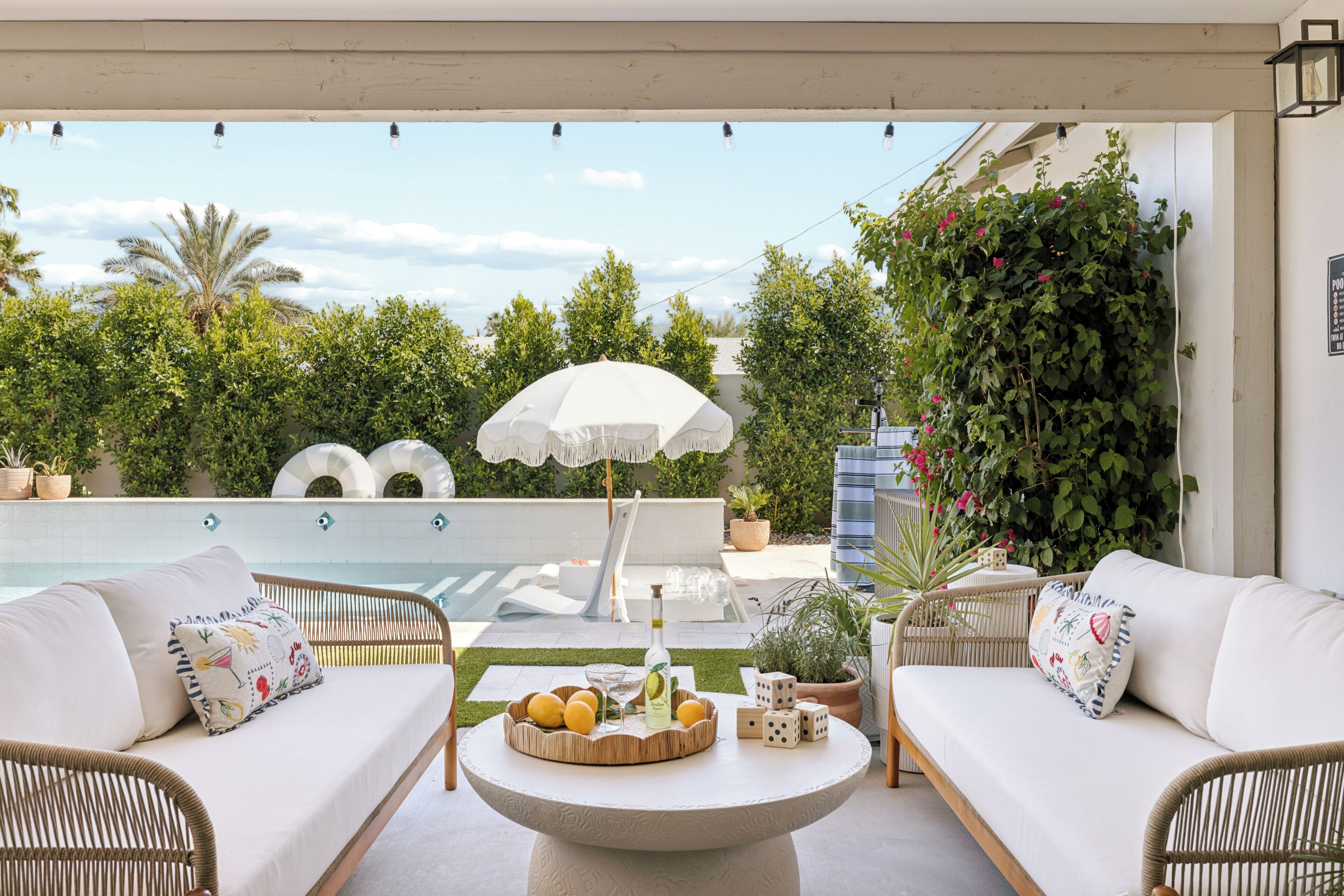 An outdoor seating area with wicker furniture, a round table with fruits and a bottle, and a white umbrella.