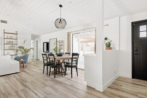 A spacious living area with a dining table, chairs, a sofa, and a black door.