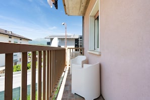 Un balcon avec une balustrade en bois, une chaise blanche et une fenĂȘtre donnant sur une rue et des montagnes.
