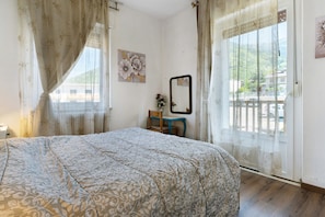 Une chambre Ă coucher avec un lit, une chaise, une petite table, un miroir et une fenĂȘtre avec des rideaux.