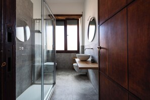 A modern bathroom with a glass shower enclosure, a wooden vanity with a large basin, and a mirror on the wall. - Dolce Vita al Colosseo (Rome)