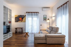 A living room with a sofa, a TV, a glass coffee table, and a painting on the wall. - Dolce Vita al Colosseo (Rome)