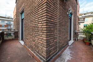 Ein Backsteinhaus mit einer gefliesten Terrasse, einer Tür und einem kleinen Gartenbereich mit Blumentöpfen.
