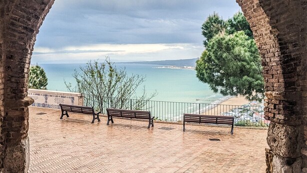 Eine gewölbte Steinstruktur mit einer Bank, einer Laterne und Blick auf das Meer.