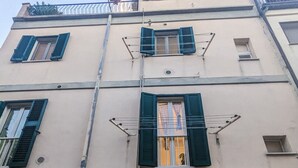 Ein mehrstöckiges Gebäude mit einem zentralen Eingang, mehreren Fensterläden und einem sichtbaren Balkon.