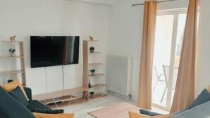 Ein modernes Wohnzimmer mit einem Flachbildfernseher, zwei Sofas, einem Couchtisch und Blick durch ein großes Fenster.