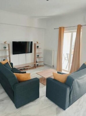 A modern living room with a flat-screen TV, two sofas, a coffee table, and a view through a large window. - Levante Breeze 2 (Zakynthos)