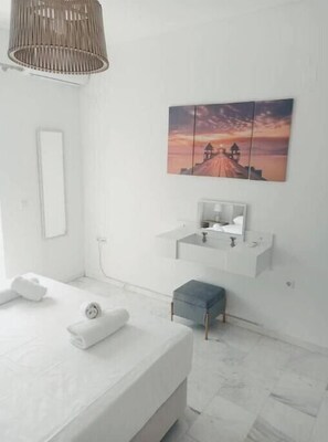 A modern bathroom with a white vanity, a hanging light fixture, and a painting of a sunset on the wall. - Levante Breeze 2 (Zakynthos)