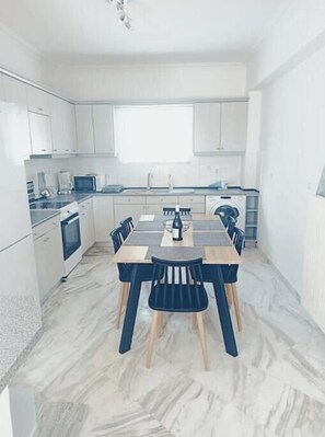 A modern kitchen with white cabinets, a dining table with chairs, and a built-in oven. - Levante Breeze 2 (Zakynthos)