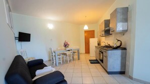Een knus woongedeelte met een bank, eettafel, stoelen, een televisie en een kitchenette.