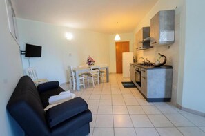 Un espace de vie compact comprenant un canapé, une table à manger, des chaises, un téléviseur et un coin cuisine.