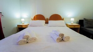 Een hotelkamer met twee bedden, elk voorzien van een houten hoofdeinde, witte lakens en twee bedlampen.