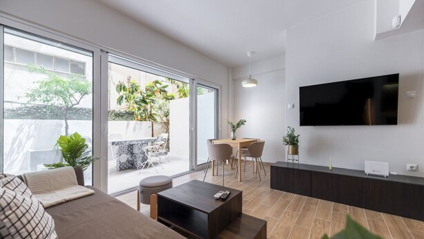 Een moderne woonkamer met een bank, salontafel, televisie en een eethoek met stoelen en een tafel.