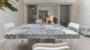 Een eetruimte met een tafel met patroon, witte stoelen en een schuifdeur naar een keuken.