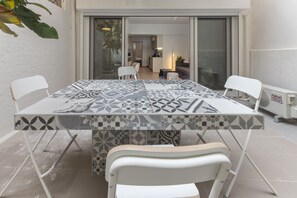 A dining area with a patterned table, white chairs, and a sliding glass door leading to a kitchen. - Phaedrus Living: Artotines Urban Residence (Athens)