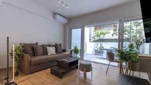 Een moderne woonkamer met een bank, salontafel en voetenbankje, een televisie en een grote schuifdeur die leidt naar een terras.