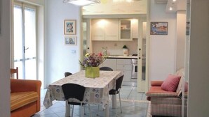 Een eetgedeelte met een tafel, stoelen, een bloemenvaas en een keuken op de achtergrond.