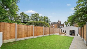 A backyard with a wooden fence, a picnic table, and a building with a brick facade. - Modern 5 bed New Cross Greenwich House (London)