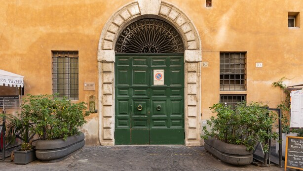 Un bâtiment doté d’une porte à double battant de couleur verte, d’un panneau interdisant le stationnement et de deux grands jardinières ornées de plantes.
