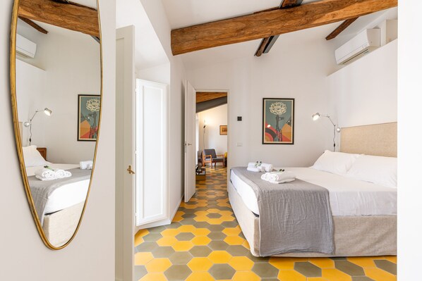 A hotel room with a mirrored wardrobe, a bed with a grey bedspread, a yellow hexagonal patterned floor, and a wooden ceiling beam. - Luxury Loft in Navona - Anima (Rome)