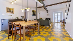 Un coin repas avec une table et des chaises en bois, une cuisine équipée d’un évier et de placards, un canapé et un sol à motifs.