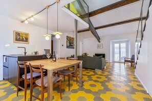 Un comedor con mesa y sillas de madera, una cocina con pileta y alacenas, un sofá y un piso con diseño.