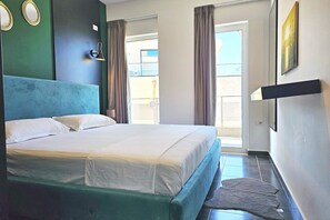 A hotel room with a bed, a wall-mounted lamp, a picture, and a view through a window. - Christine Sunny Corner 004 /w Sea View Balcony (Sarandë)