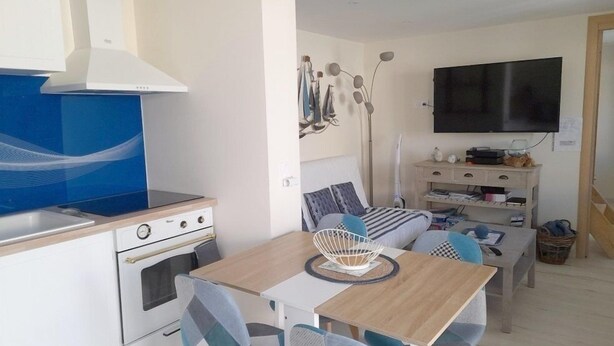 A compact living space with a kitchenette, a dining area, a TV mounted on the wall, and a staircase leading to another level. - Gîte Nath & Steph 5 classified 3*** in Cayeux sur Mer - Baie de Somme (Cayeux-sur-Mer)