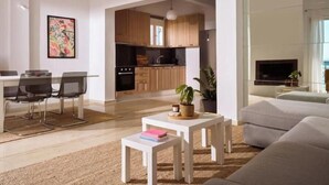 Een moderne woonkamer met een bank, een eethoek met stoelen, een keuken met houten kastjes, en een aan de muur bevestigde televisie.